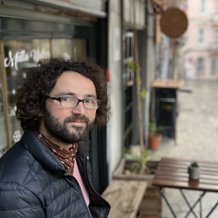 Photo of Anil Askin sitting at a cafe along a city street.