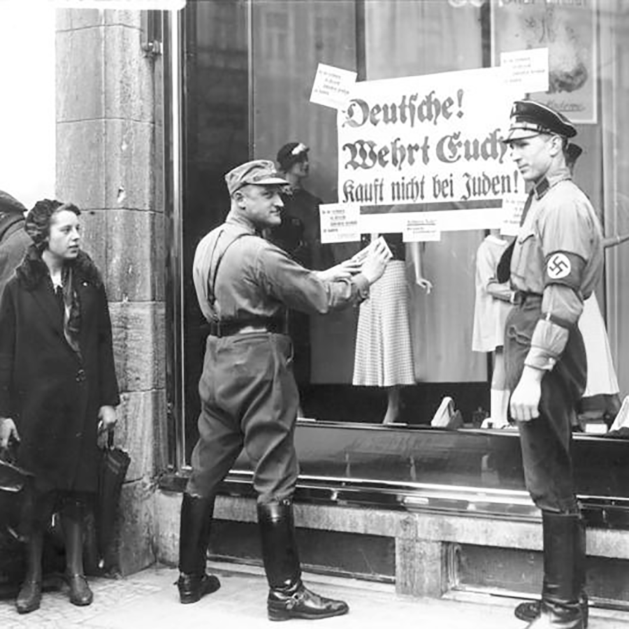 Black and white photo of two Nazis posting boycott signs on a store window as a woman looks on.